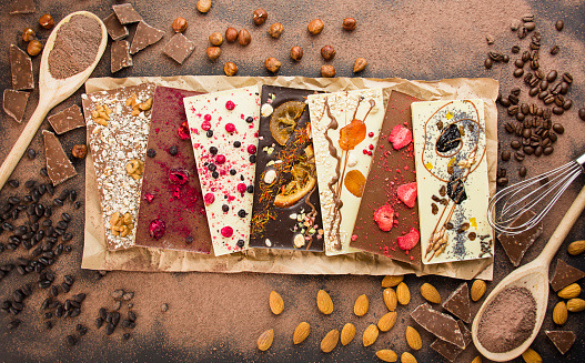 Handmade chocolate with berries, nuts, dried fruits and ingredients for making chocolate on a dark background. Black and white chocolate. Chocolate bars. Close-up. Chocolate background. Culinary background.