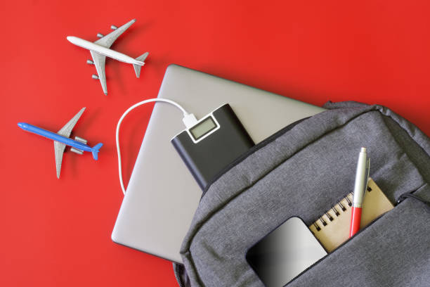 istock Gray backpack with gadgets: laptop, mobile phone, power bank, notepad and pen on red background next to toy airplanes. Concept of gadgets and luggage of students, IT people and journalists. 1433473549