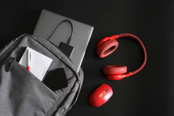 istock Gray urban backpack with laptop, mobile phone, external ssd disk, notepad and pen lies on black table next to red headphones and mouse. Study and lifestyle with gadgets. Freelance tools. 1433473593
