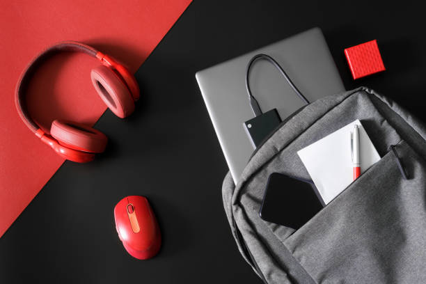 istock Urban gray backpack with laptop, notepad, pen, phone and external ssd drive on a red and black table next to red headphones and a mouse. Study and lifestyle with gadgets. Freelance tools. 1433473608