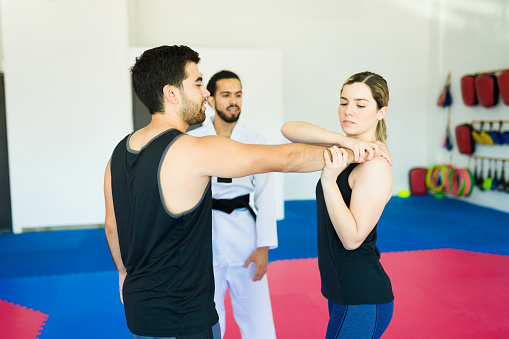 Young woman and man taking a self-defense class and fighting at a martial arts school