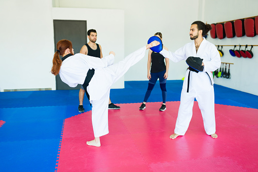 Black belt taekwondo female student kicking and training with a martial arts coach