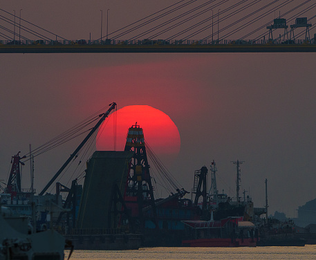 Sun just on top of the floating crane and under Ting Kau Bridge during the sunset