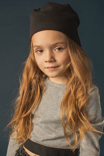Redhead girl in warm autumn clothes in studio on dark blue background. Little girl with long hair in t-shirt and hat. Portrait
