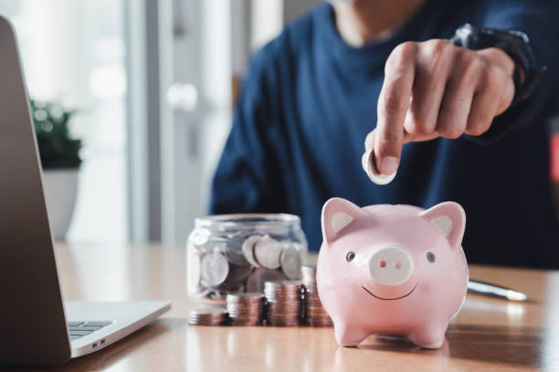 hand putting coins in a piggy bank for save money and saving money concept. - household equipment light bulb compact fluorescent lightbulb lighting equipment imagens e fotografias de stock