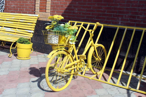 a yellow decorative bicycle with flowers stands in a parking lot on a summer day. - ретро imagens e fotografias de stock