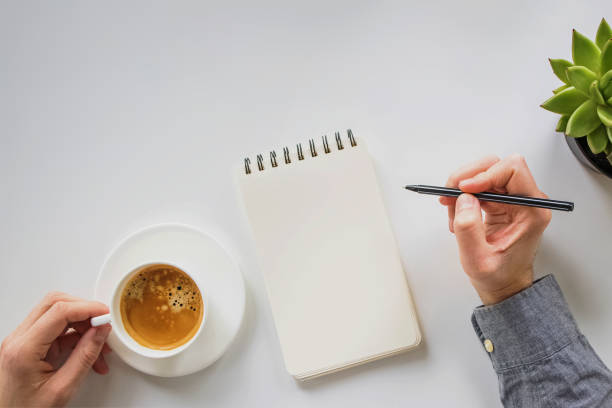 istock Paper notepad mock-up. Man holding a pen and a coffee, top view 1433494323