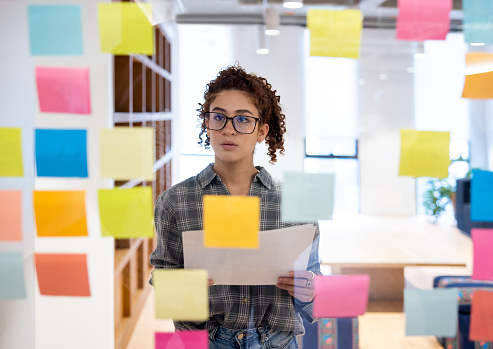 Young woman brainstorming while working at a creative office and using adhesive notes on a board