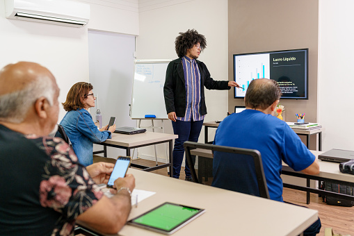 Female High School Teacher Standing Next To Interactive Whiteboard And Teaching Lesson To Pupils Wearing Uniform