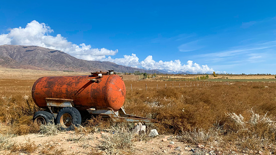 Rural landscape with mountains and a gas tank on a field in the foreground