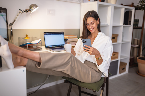 Photo of happy young woman using her smart phone while working from home