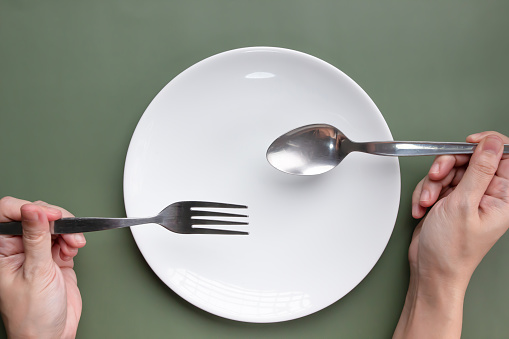 Woman hand holding spoon and fork with white plate which read for eating for breakfast, lunch and a dinner.