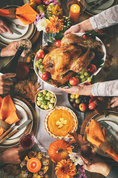 Group of friends or family celebrating together at festive turkey dinner table. Thanksgiving celebration traditional dinner concept. Roasted turkey on a rustic table decoraded with pumpkins, vegetables, pie, flowers and candles stock photo