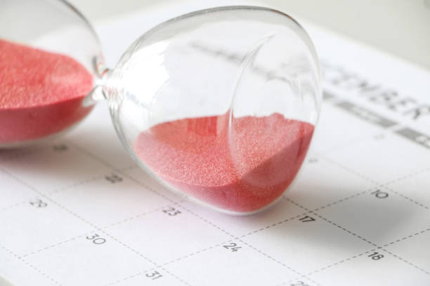 istock Hourglass with red sand on its side, on calendar, signifying pause in time, time out, taking a break, need more time 1433545160