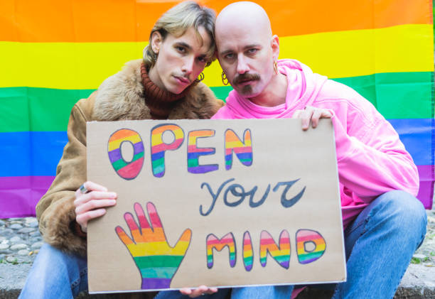 Homosexual gay couple showing his banner at lgbt pride parade outdoor with rainbow flag background Homosexual gay couple showing his banner at lgbt pride parade outdoor with rainbow flag background School Crossdressing stock pictures, royalty-free photos & images