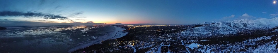 A panoramic view of Anchorage, Alaska between the sea and snowy mountains at sunset