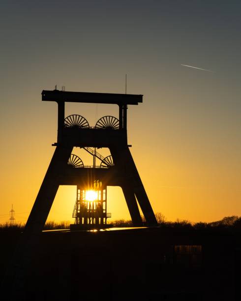 istock Bright sun in yellow sunset sky shining behind a mining tower in the field 1433549102
