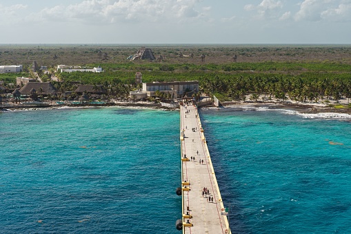 An aerial view of a bridge over a clear ocean with trees on the coast