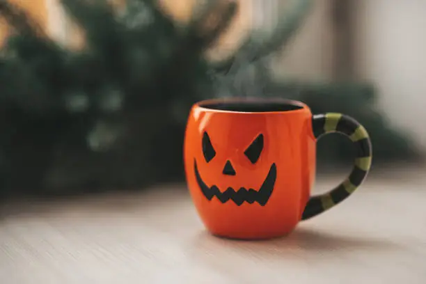 Photo of Clouse up of cup in shape of pumpkin Jack O lantern with hot coffee on windowsill