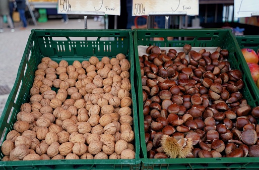 A closeup of fresh dark and light brown chestnuts and walnuts in plastic boxes at a market