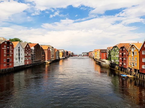 A lovely view of Trondheim, Norway with colorful little houses on either side of a river under a cloudy sky