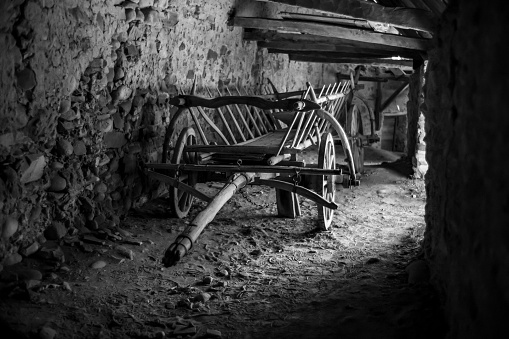 A monochrome shot of a wooden cart against the stone wall