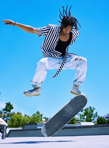 Cool young, stylish african american boy performing skate tricks on his board at the skate park. Focused young man performing ollies on his skateboard at the park outside. Serious man enjoying skating