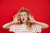 Portrait of surprised teenage girl with long fair hair, open mouth wearing white T-shirt, raising hands with open palms.