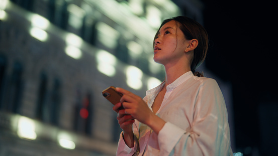 A young woman is using her smart phone in the city at night.