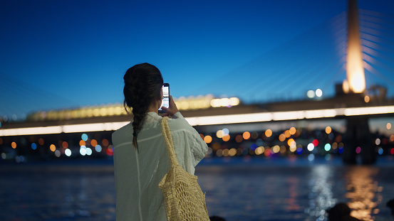 A young female tourist is taking photos of the cityscape in the city at night.