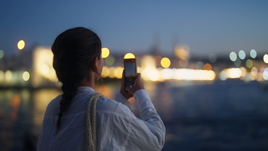 A young female tourist is taking photos of the cityscape in the city at night.