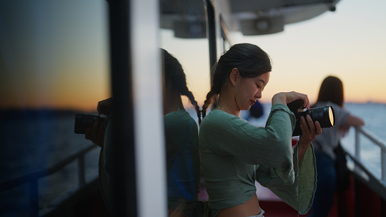 A young female tourist is enjoying traveling on a ferry and taking photos and videos during her travel.