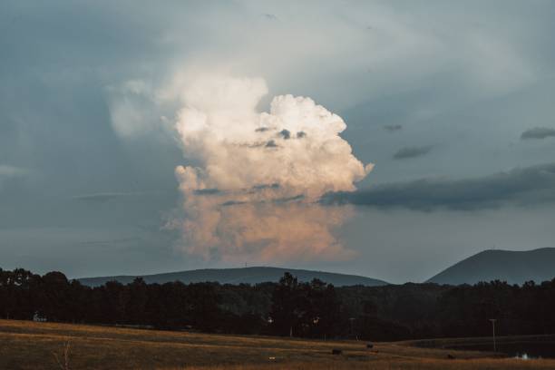 A big white cloud in a gloomy stormy sky over mountains and fields with green trees