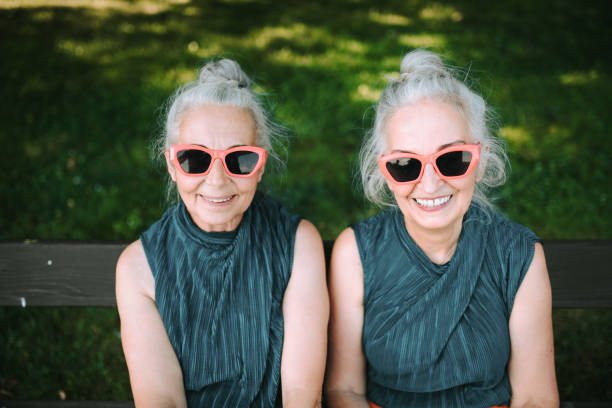 high angle view of happy senior women, twins in same clothes, smiling and posing in city park. - eeneiige tweeling stockfoto's en -beelden