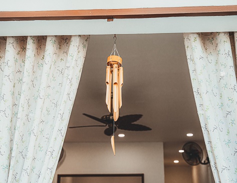 A low-angle of dark wind chimes bamboo with curtains on both sides and ceiling design in the background