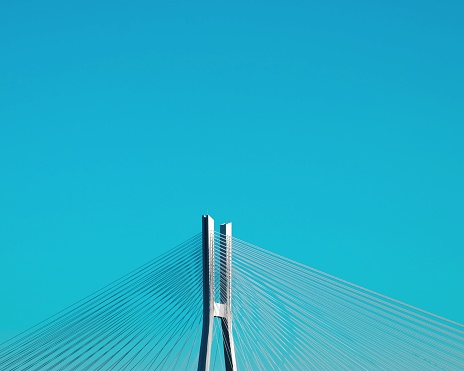 A vertical shot of the bridge tower with suspender cables against the background of the blue sky.