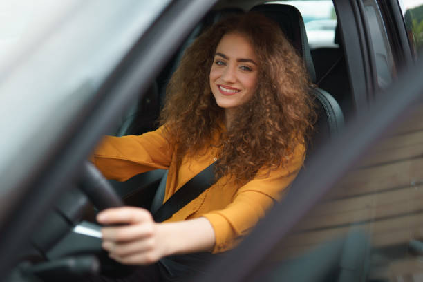 Young woman driving a car in the city. Portrait of a beautiful woman in a car, looking out of the window and smiling. stock photo