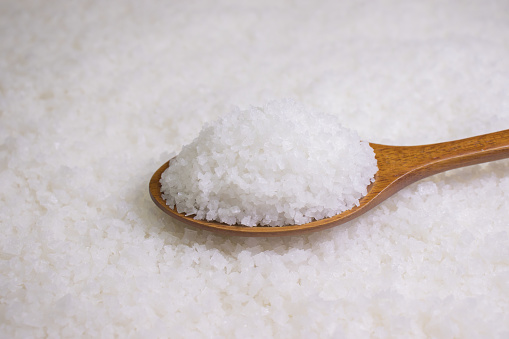 Salt in wooden spoon on salt background.