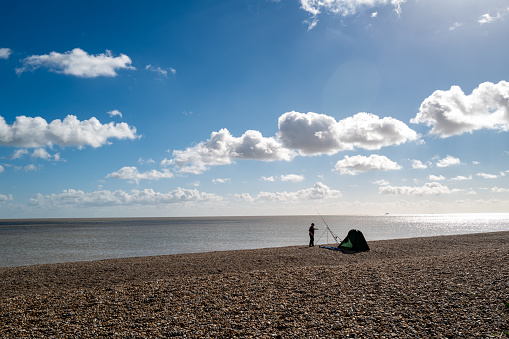 Distant view of a sea fisherman with his beach tent, looking to catch Bass. A day tent is seen, to help protect a coming storm.