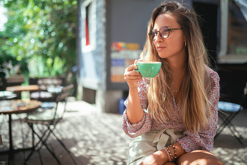 Gorgeous woman sitting in a café garden and drinking coffee