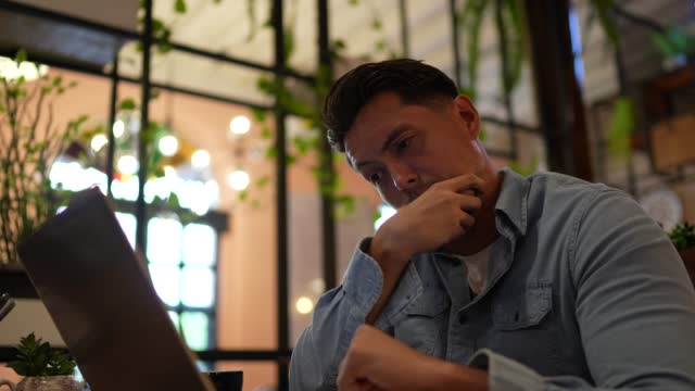 Worried mid adult businessman using laptop in a coffee shop