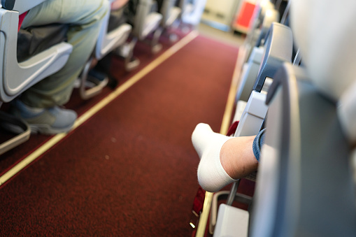 Action of an airplane passenger is crossing legged sitting at the economy class, with narrow corridor as blur background. People in transportation action, close-up and selective focus at heel part.