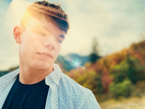 Portrait closeup teenage male looking down in thoughtful contemplation, dusk autumn sunlight cascading over face. Contented emotion. Mental health and wellness.