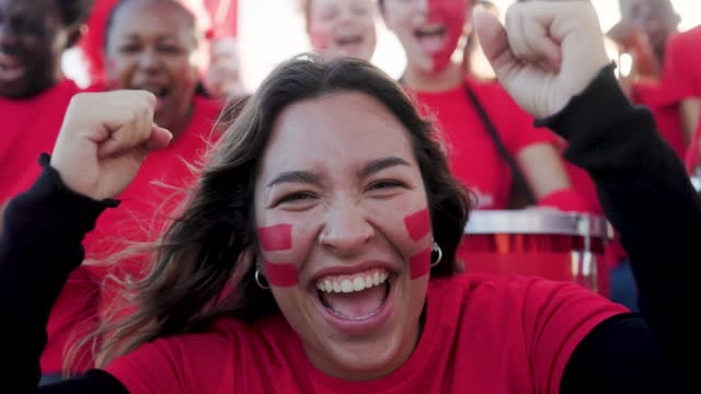 Hispanic football fans celebrating and supporting their red sport team watching the game on stadium tribune - Soccer supporters screaming during world championship event