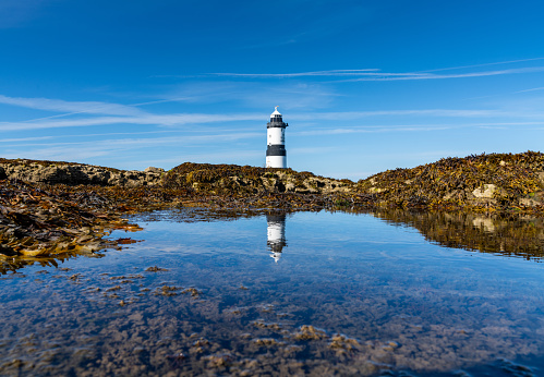 A view of the Penmon Lighthouse in North Wales with reflections in a tidal pool