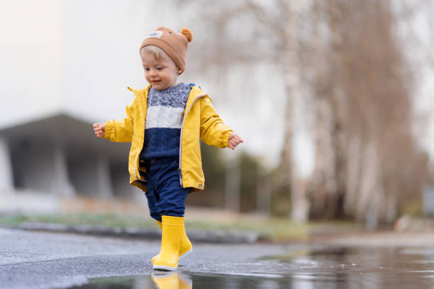 가을 날 비가 내린 후 웅덩이에서 뛰어 내리는 노란 비옷을 입은 행복한 어린 소년. - puddle rain child splashing 뉴스 사진 이미지