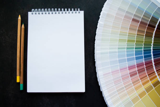 istock Fan paint samples interior design painting. Multicolored natural colors. Black background, white notebook for copy space and pencils 1433638755