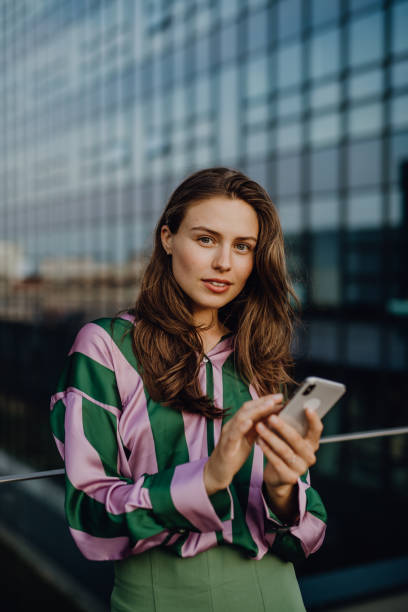 Portrait of beautiful young woman with smartphone outdoor in city, during sunset. stock photo