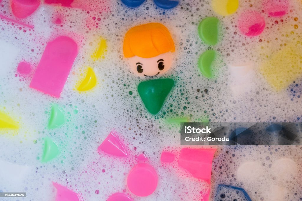 Washing of children toys, plastic building blocks with figurines. A smiling little fellow and colorful cubes float in the foaming water Washing of children toys, plastic building blocks with figurines. A smiling little fellow and colorful cubes float in the foaming water. The concept of hygiene, cleanliness. Safety and disinfection Action Figure Stock Photo