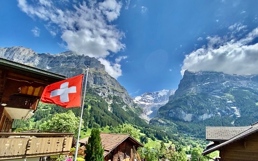 one bright red swiss national flag blows proudly in the sunshine of the alpine village of grindelwald, switzerland.
